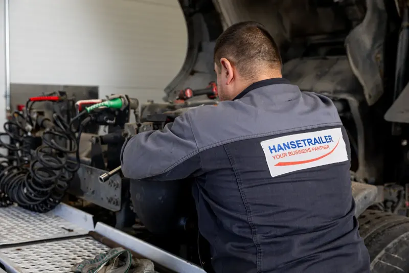 Ein Mechaniker in HTL-Arbeitskleidung arbeitet an Achse und Bremse eines Aufliegers