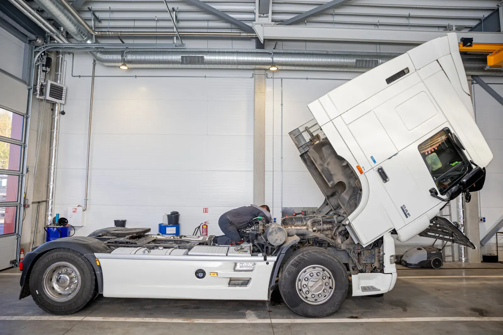 Zugmaschine mit gekipptem Fahrerhaus in der HTL-Werkstatt; ein Mechaniker arbeitet am Motor
