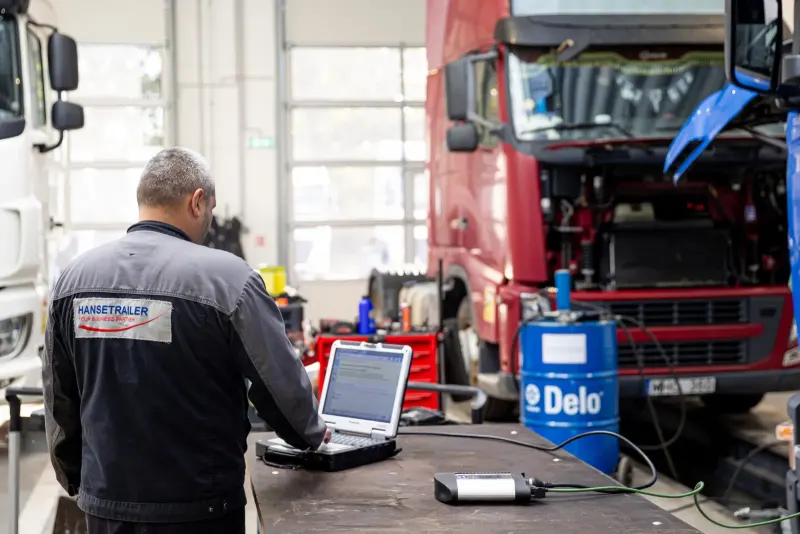 Ein Mechaniker führt am Laptop die Diagnose an einem roten Lkw durch